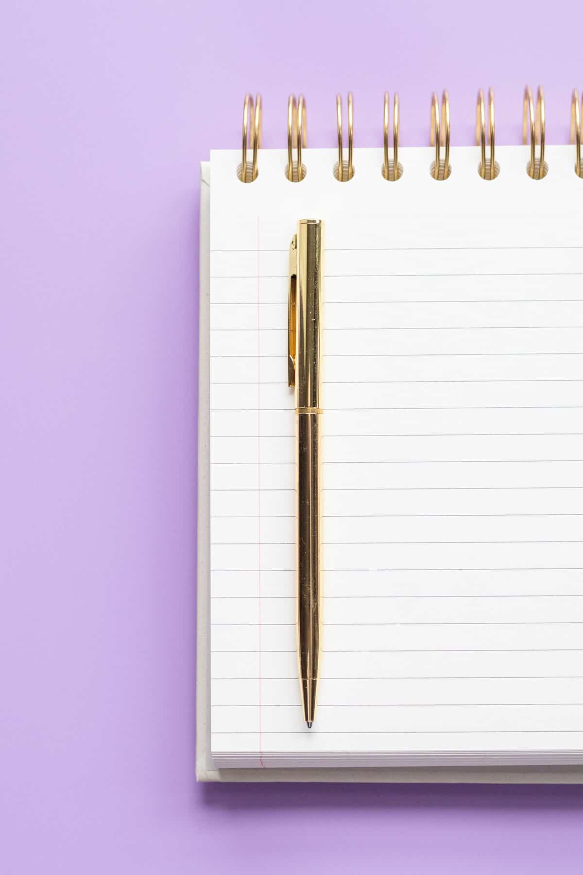 Notizblock mit goldenem Stift auf lila Hintergrund
